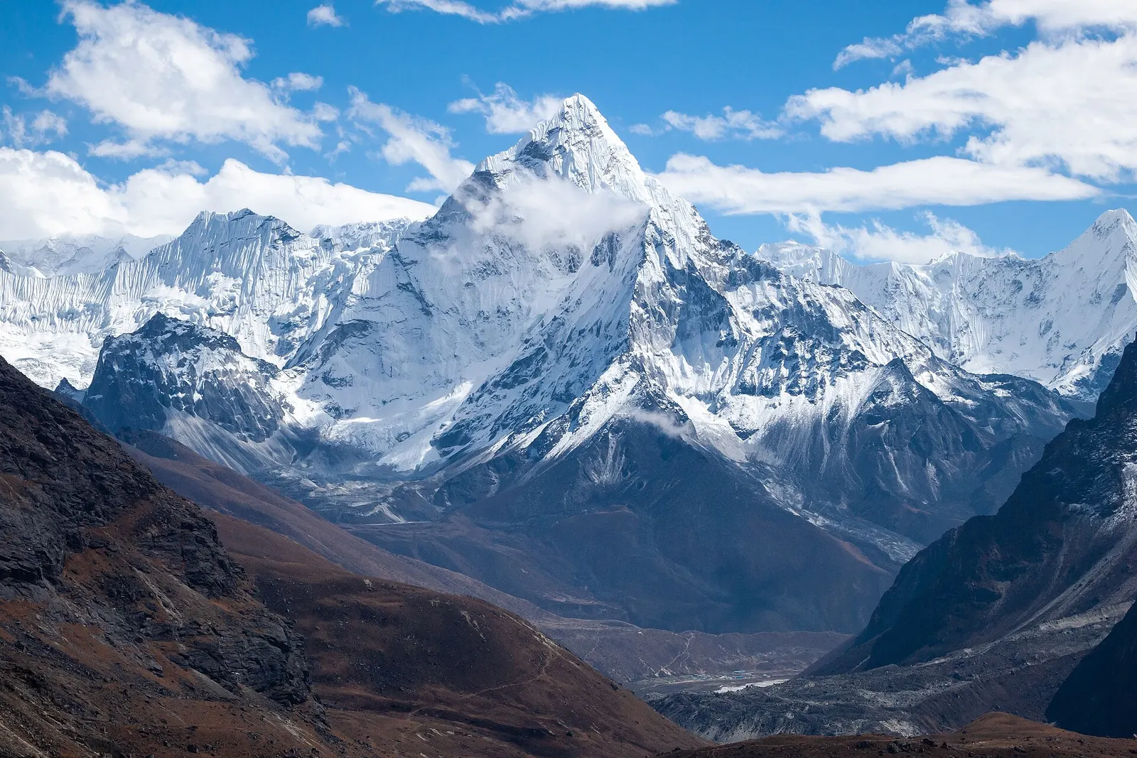 Ama Dablam's sharp snow-covered summit rising above a deep valley in the Khumbu region under blue sky and clouds