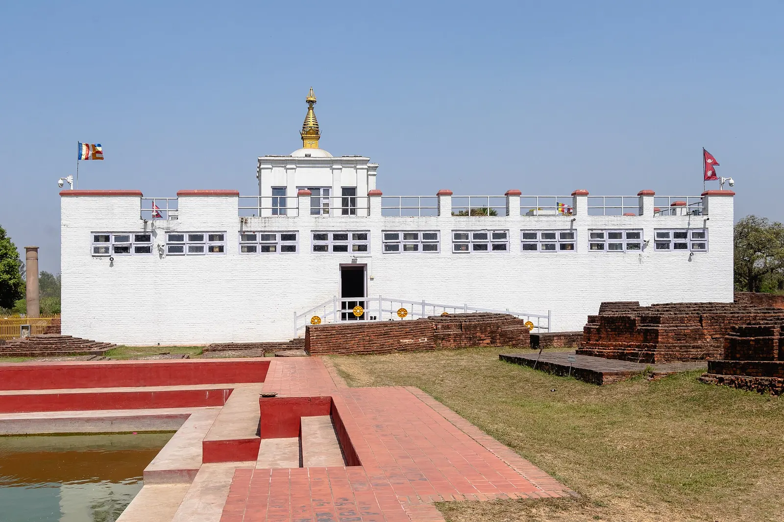 The white Maya Devi Temple at Lumbini with brick ruins and a red-brick pool in the foreground