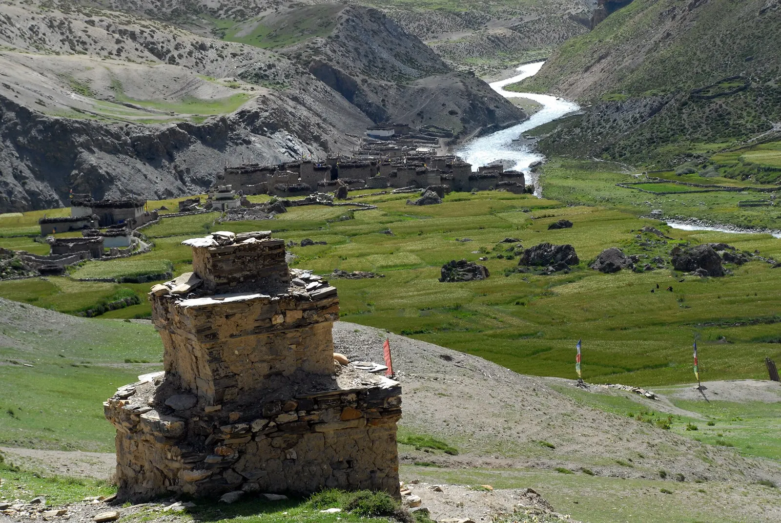 A stone chorten above the green fields of Chharka Bhot, with the village and a river below bare mountains.