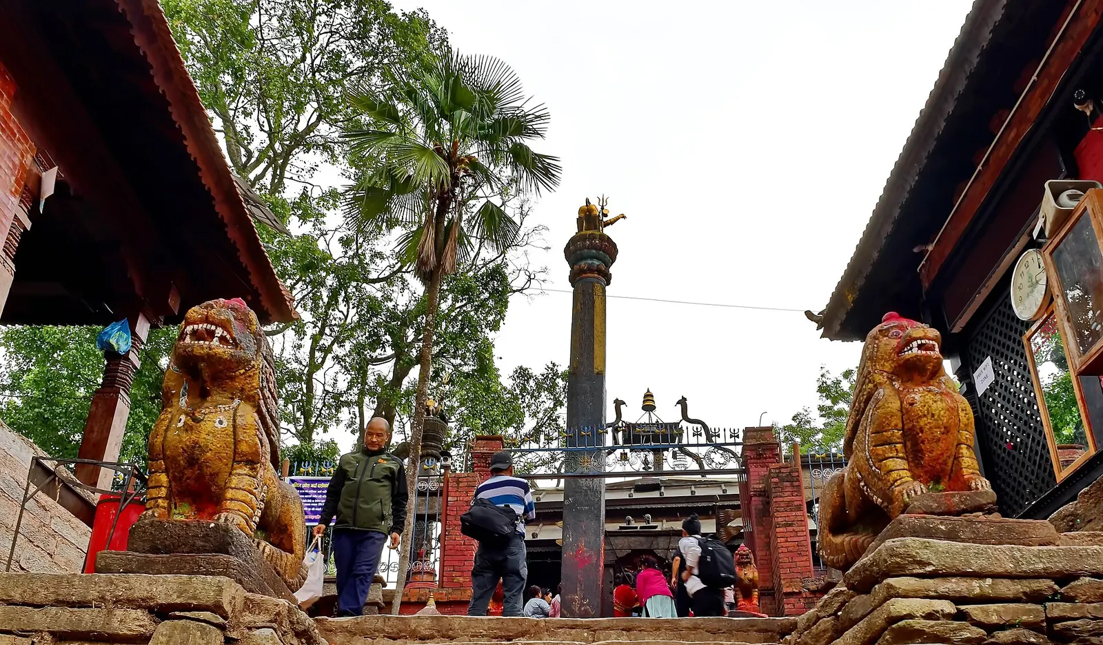 Stone lion guardians and a tall pillar at the entrance to the Dolakha Bhimsen temple.