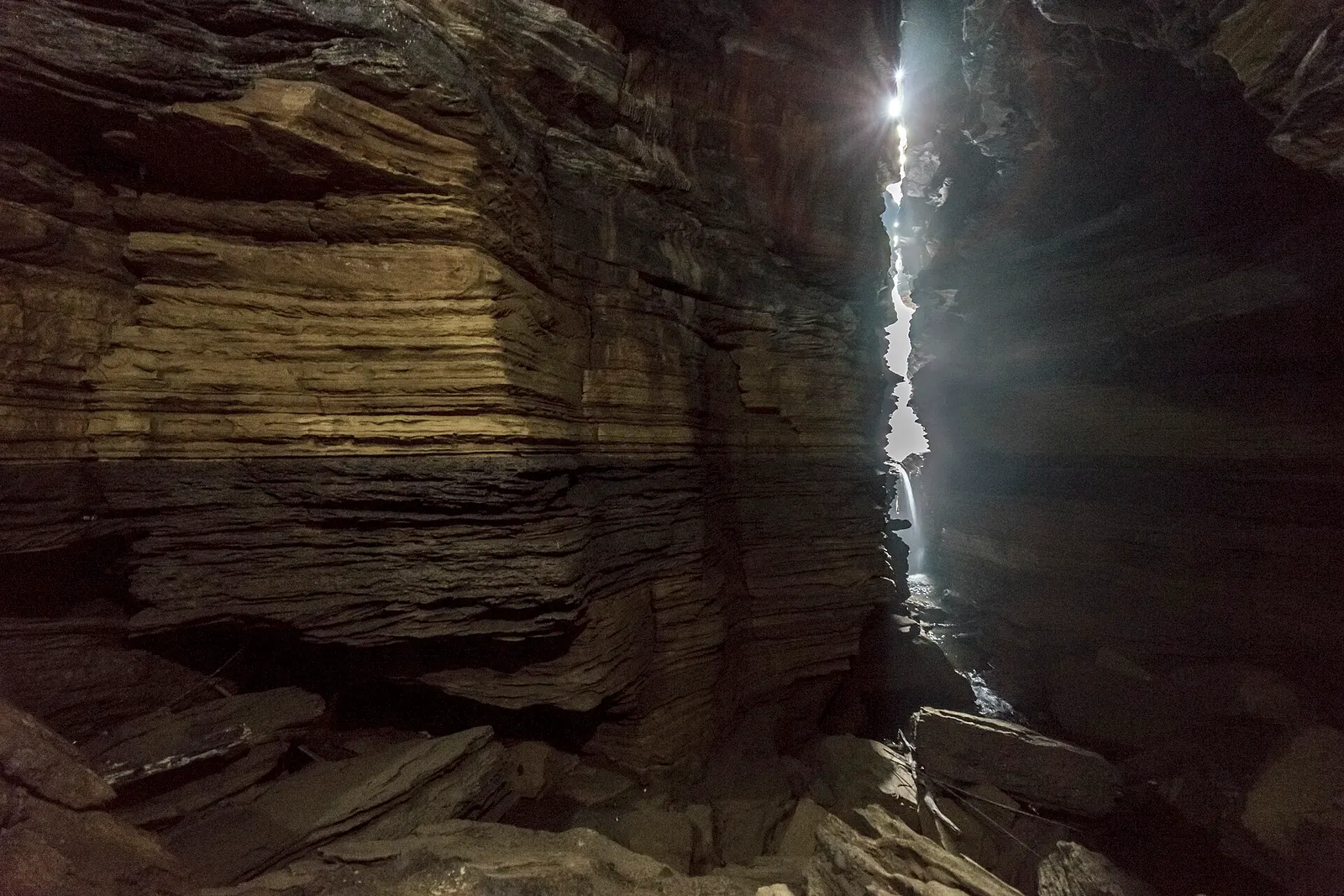 A narrow cleft of daylight between dark, layered rock walls deep inside Gupteshwor Cave.