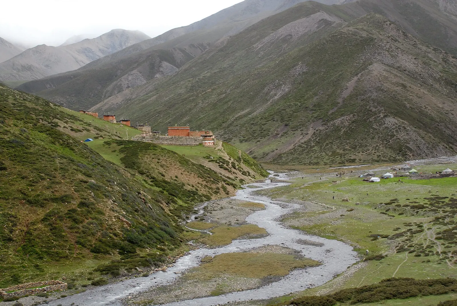 Red-painted buildings on a green slope above a braided stream near Saldang in Upper Dolpo.