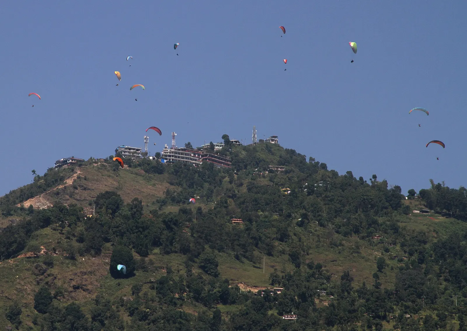 Paragliders drifting over the hillside below the Sarangkot viewpoint above Pokhara.