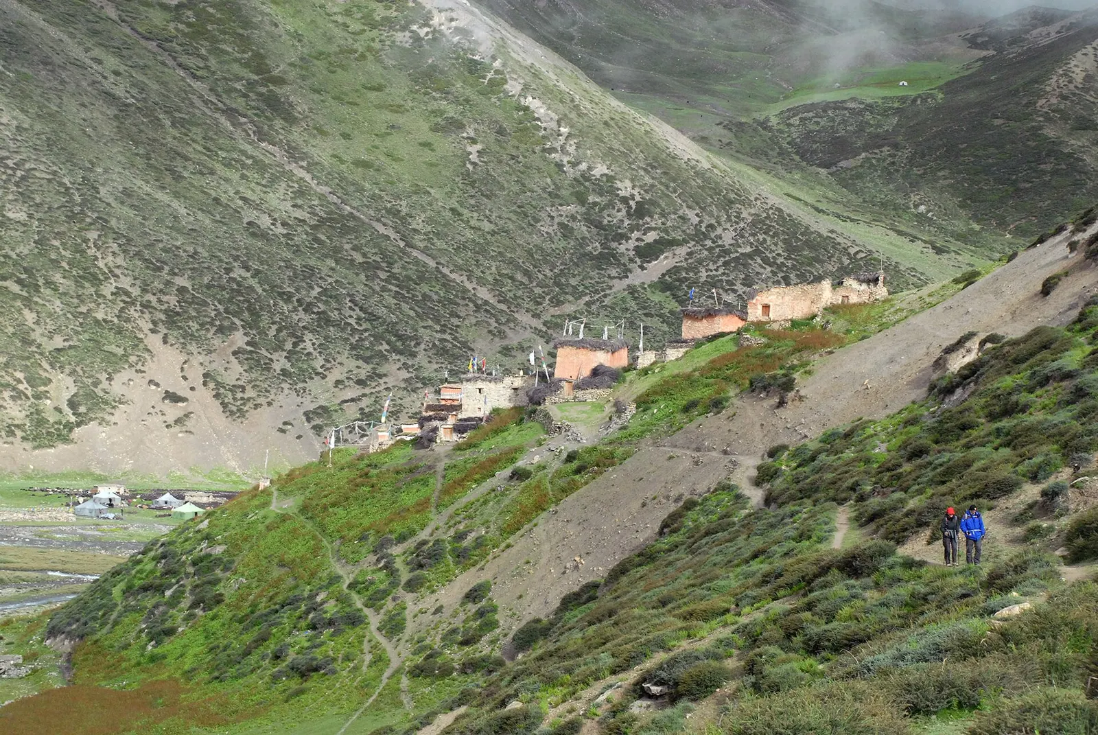 Red-painted monastery buildings of Shey Gompa on a green hillside above a valley in Upper Dolpo.