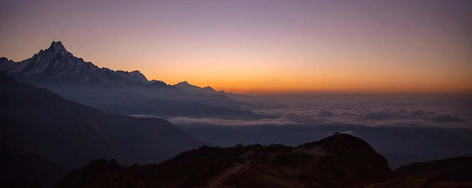 Dawn colours behind the silhouette of Machhapuchhre and a sea of cloud, seen from Muldai viewpoint.