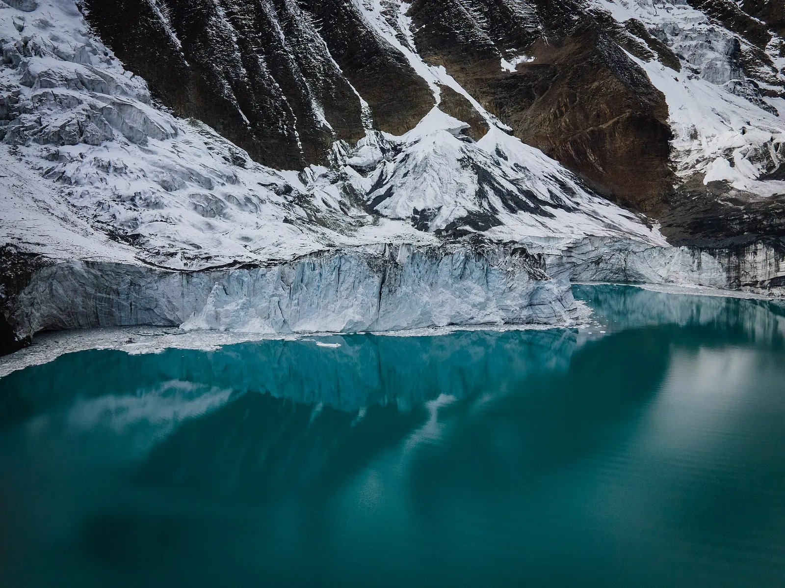 Turquoise water of Tilicho Lake reflecting the ice cliff of the Tilicho glacier and snowy slopes above it.
