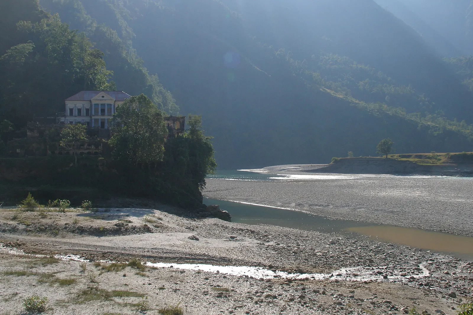 Rani Mahal seen from a distance on a forested bluff above the wide, stony Kali Gandaki riverbed.