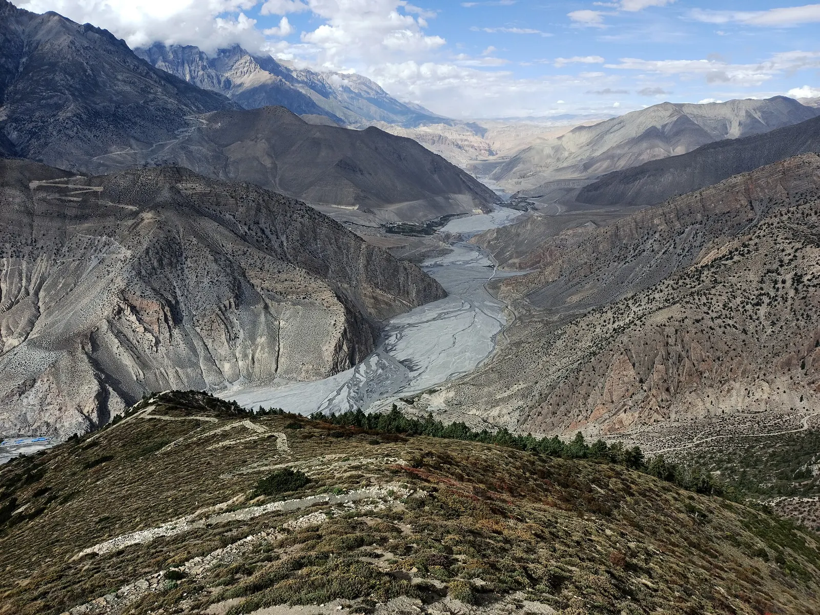 A wide, braided river valley winding between barren grey mountains in Mustang